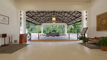 A covered outdoor area with a metal roof, a wooden bench, a potted plant, and a sign with a logo.