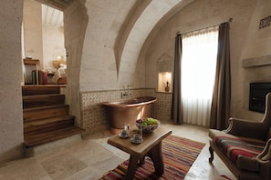 A spacious room with a large bathtub, a wooden bench, and a sofa. - Cappadocia Cave Suites (Nevsehir)