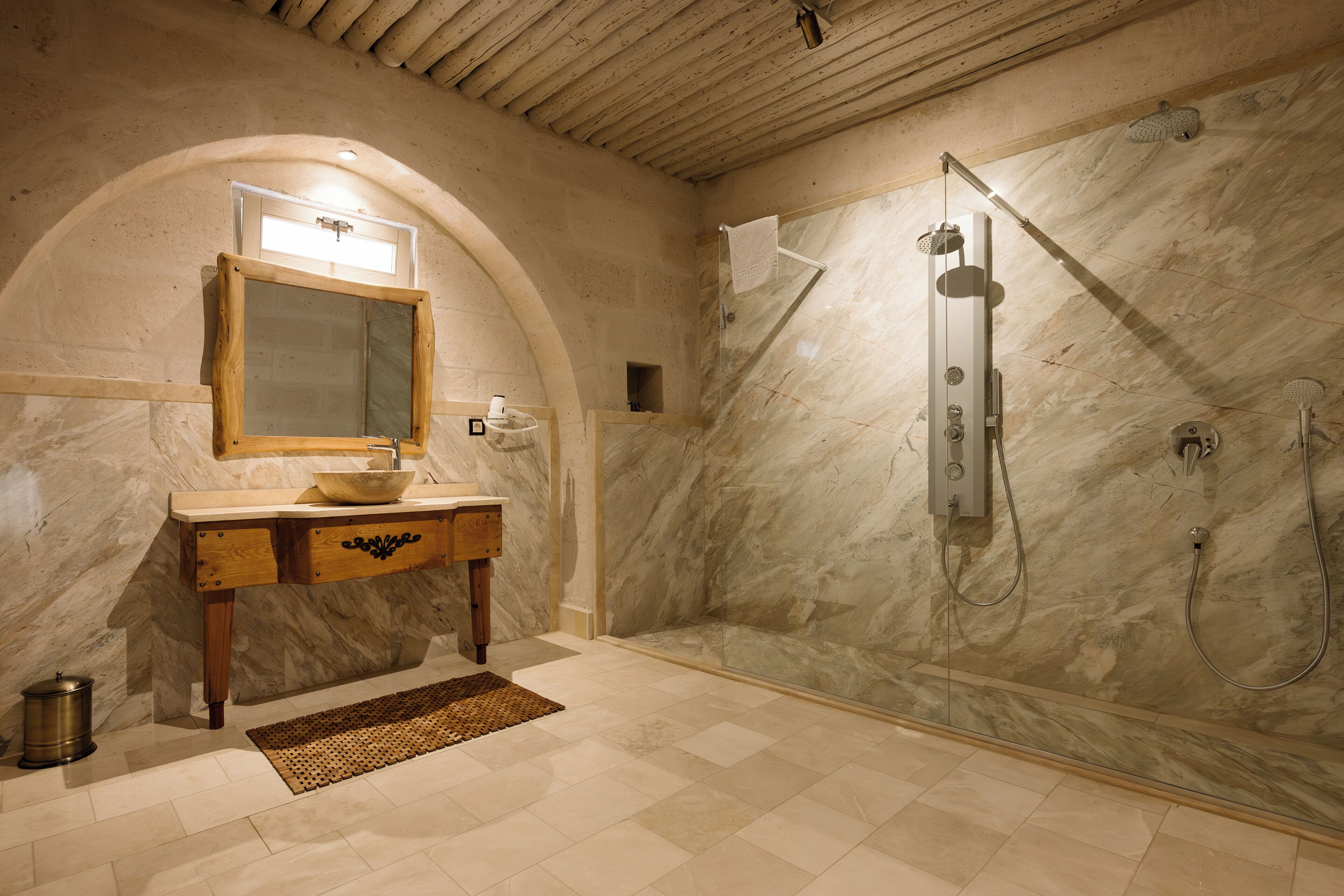 A bathroom with a marble vanity, a wooden sink, a glass-enclosed shower, and a tiled floor.