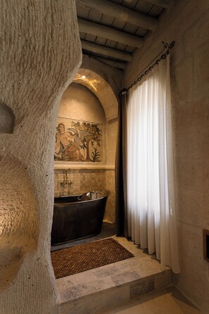 Eine Steinsäule mit Mosaik, einer Badewanne und einem Fenster mit Vorhängen.