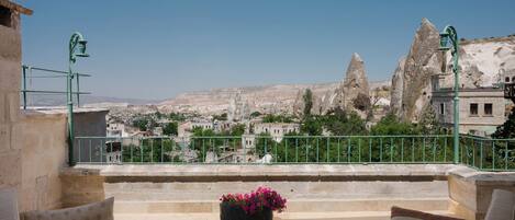 A terrace with outdoor seating, a flower pot, and a view of a town with distinctive rock formations.