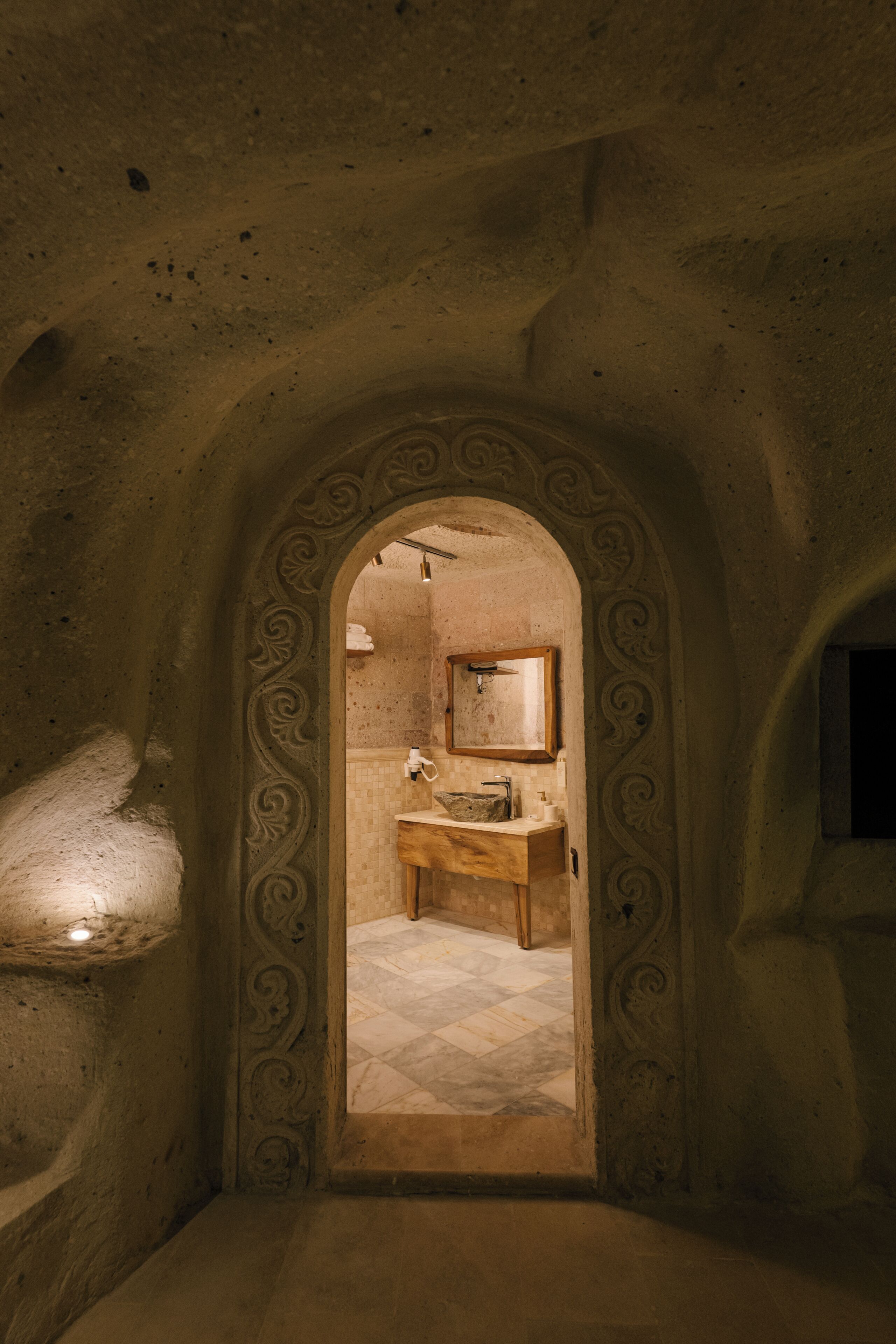 An arched doorway leading to a bathroom with a stone sink, a mirror, and a towel rack.