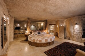 Ein rundes Bett mit karierter Bettdecke in einem Zimmer mit Steinsäulen, einem Kamin und einem Holztisch mit Stühlen.