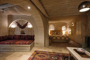 A cozy, rustic room with a stone wall, a bed with patterned bedding, a sofa with cushions, a patterned rug, and a table with a bowl.