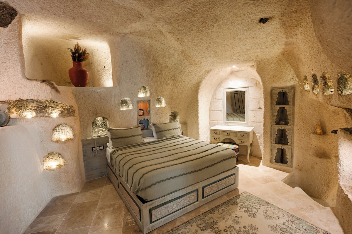 Un dormitorio con pared de piedra, cama, cómoda y espejo.