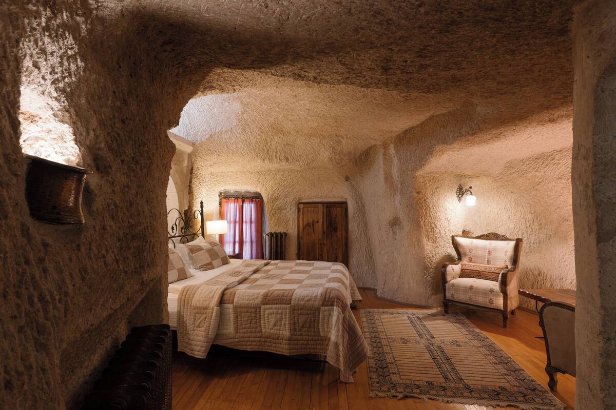 Un dormitorio rústico con pared de piedra, cama de madera, una silla y una lámpara.