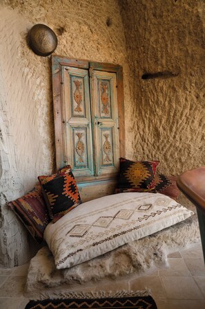 A rustic room with a stone wall, a wooden door with intricate carvings, and a bed with patterned pillows.