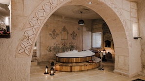 Een wellnessruimte met een houten jacuzzi, stenen muren en een decoratieve boog.