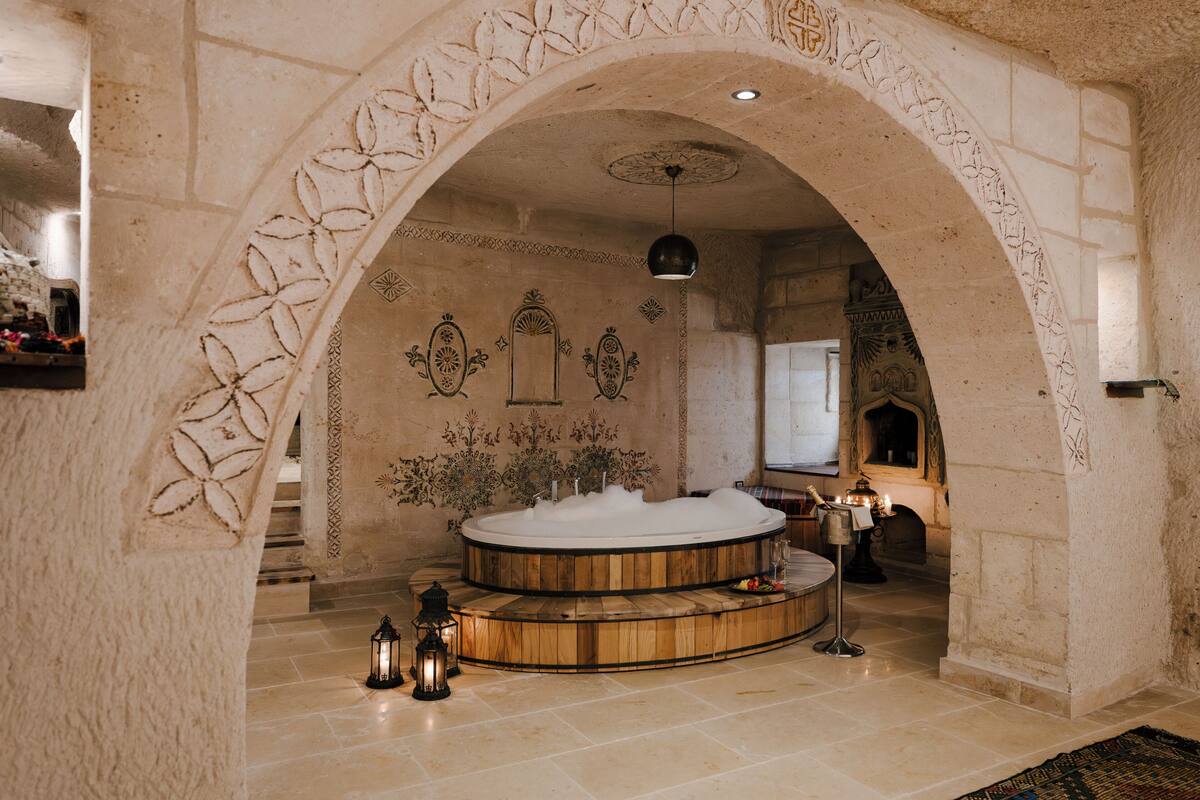 Un área de spa con un jacuzzi de madera, paredes de piedra y un arco decorativo.