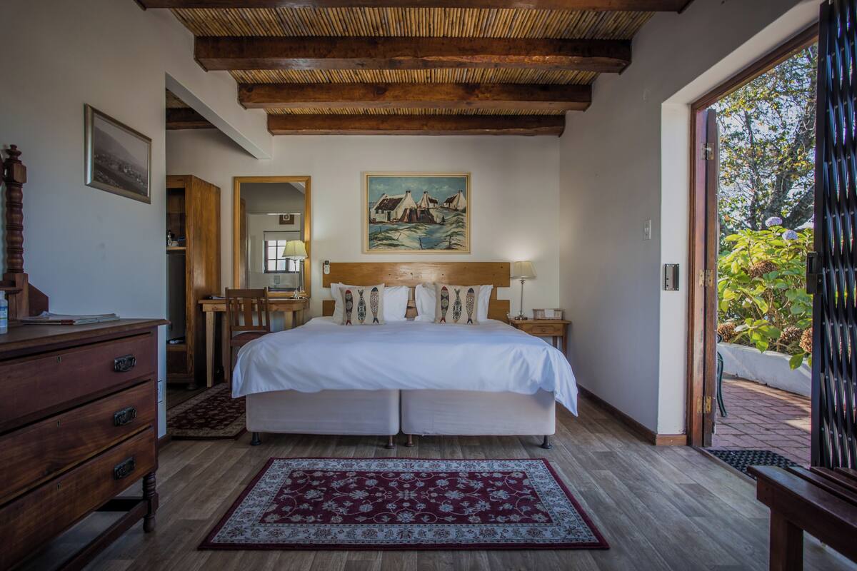 Un dormitorio con techo de madera, una cama grande con ropa blanca, un aparador de madera, una mesita de noche y un cuadro en la pared.