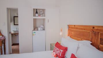 A hotel room with a wooden headboard, white bedding, a red pillow with the word "BRIGHT," and a minibar with various items.