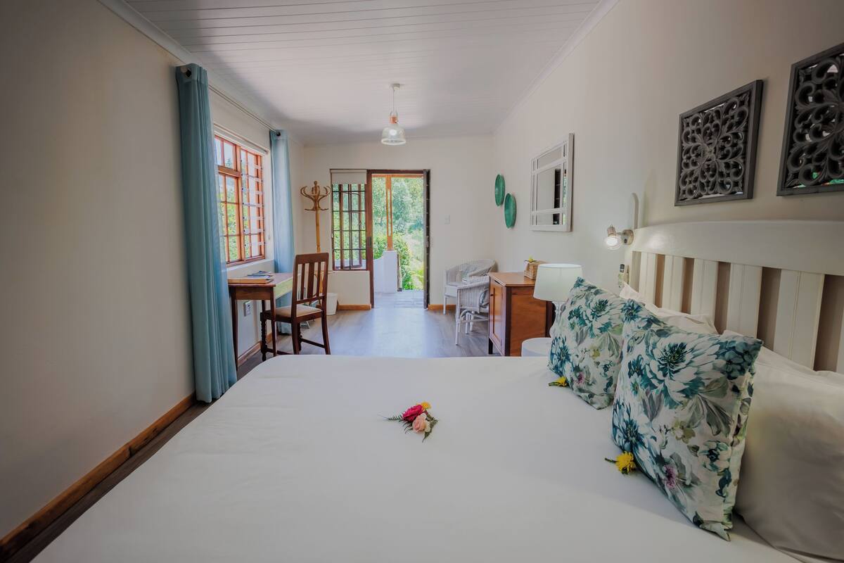 Un dormitorio con cama, escritorio y silla. Hay una ventana con cortinas, una puerta que da al exterior y una lámpara en el techo.