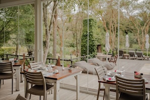 An outdoor dining area with wooden tables and chairs, surrounded by greenery and trees. - Aan de Oever Guesthouse (Swellendam)