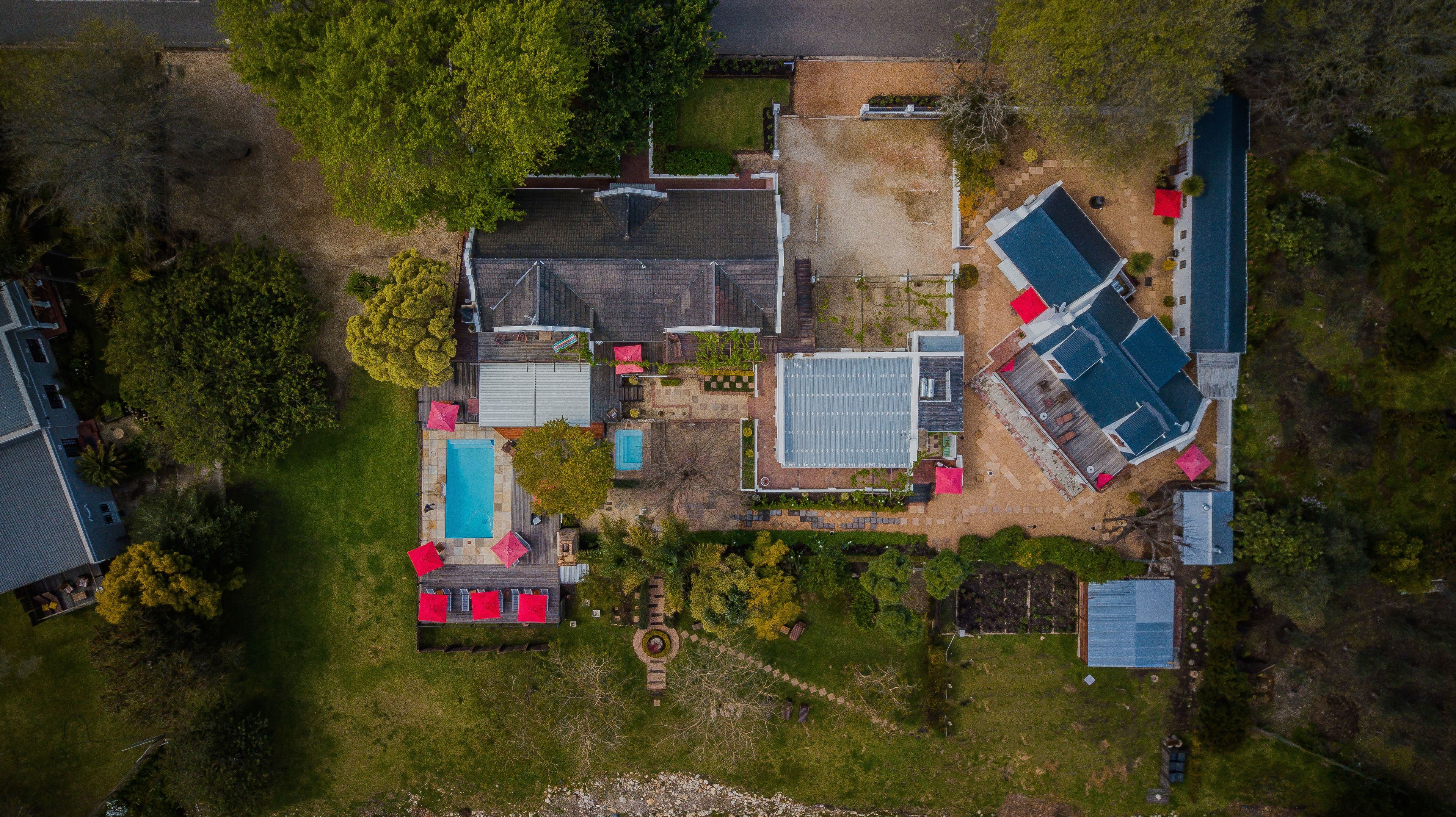 Luchtbeeld van een woongebied met een zwembad, een tennisbaan en een groot huis met een schuin dak.