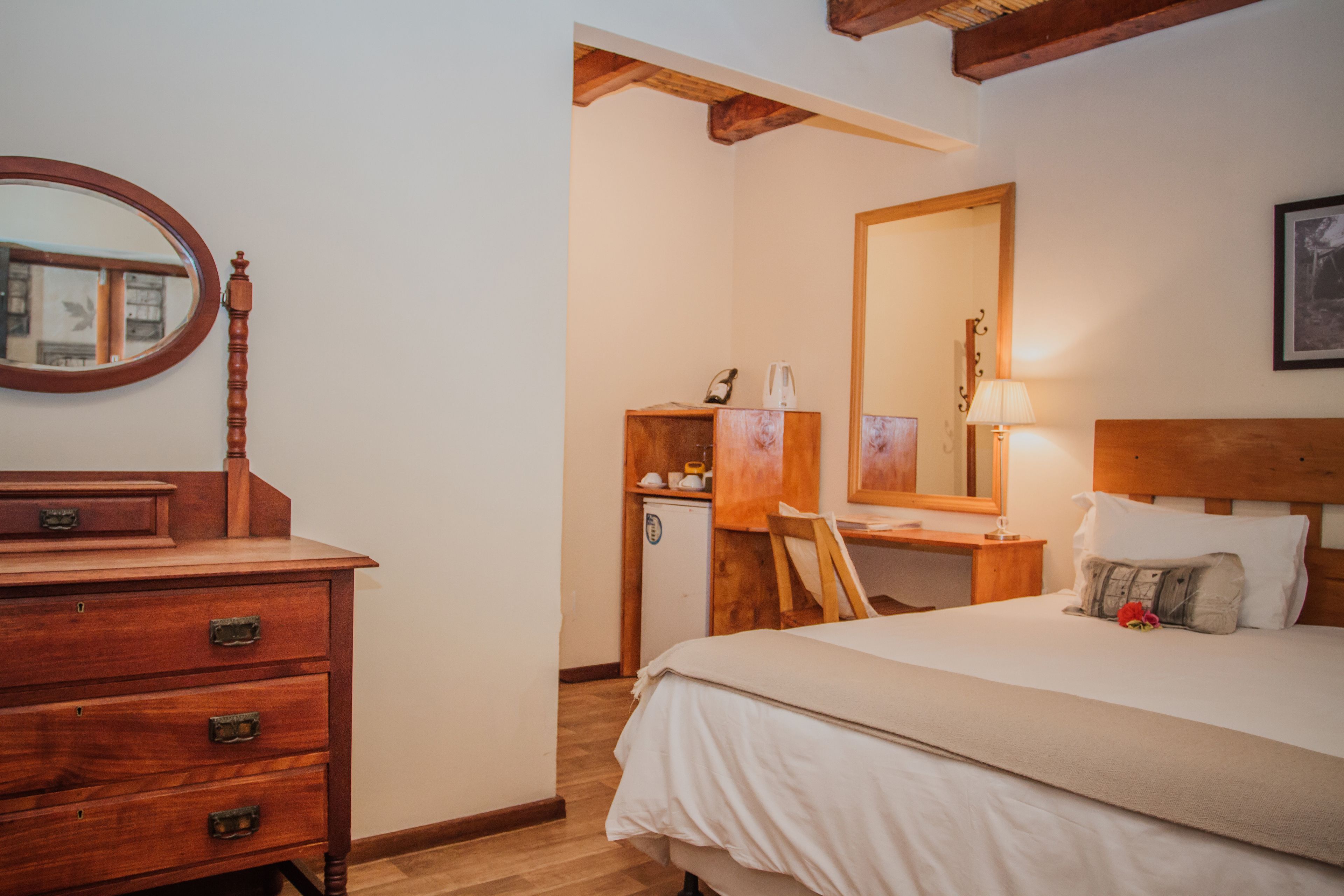 Ein Schlafzimmer mit einem Holzkapfenster, einem Schreibtisch, einem Bett mit Kopfteil, einem Spiegel und einer Lampe.