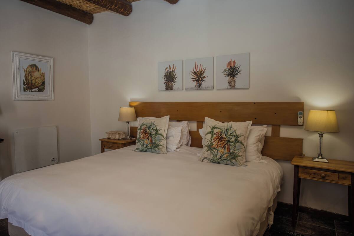 Una cama bien hecha con almohadones florales, un cabecero de madera y dos lámparas de noche.