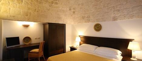 Hotelkamer met een stenen muur, een bed met witte lakens, een bureau met een computer en een stoel.