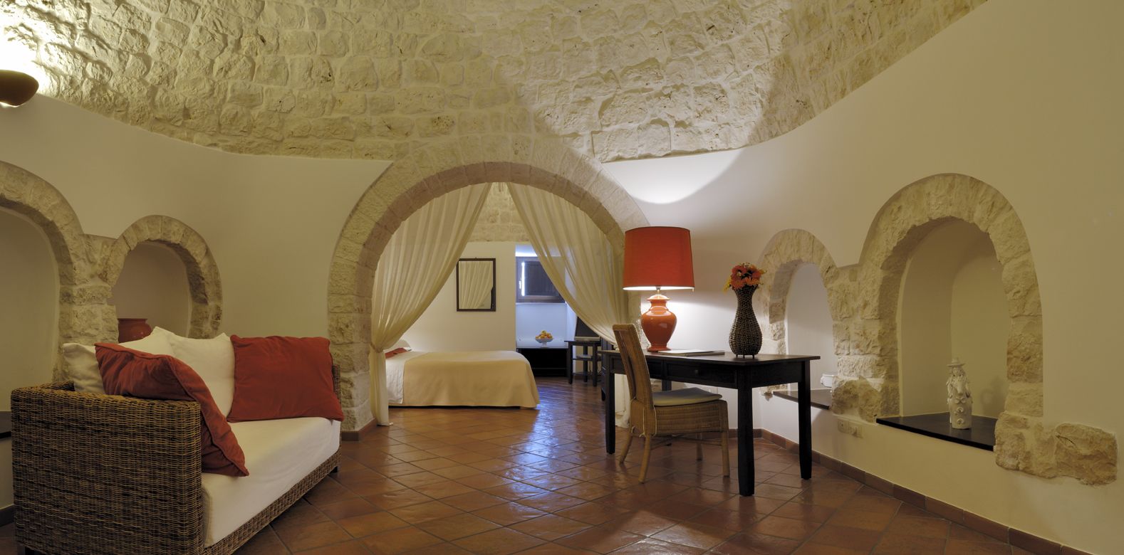 Una habitación acogedora con un sofá de mimbre, una mesa de comedor con un florero y arcos de piedra.