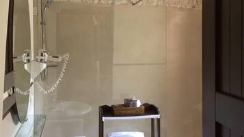 Un baño con pared de piedra, un lavamanos blanco, una cabina de ducha de vidrio y un estante con toallas.