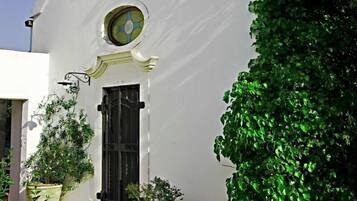 A white building with a black door and a round window, surrounded by greenery.