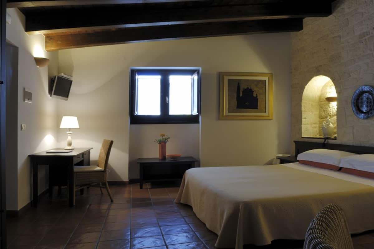 Ein Schlafzimmer mit einem Bett, einem Schreibtisch, einem Stuhl, einem Fenster und einem an der Wand befestigten Fernseher.