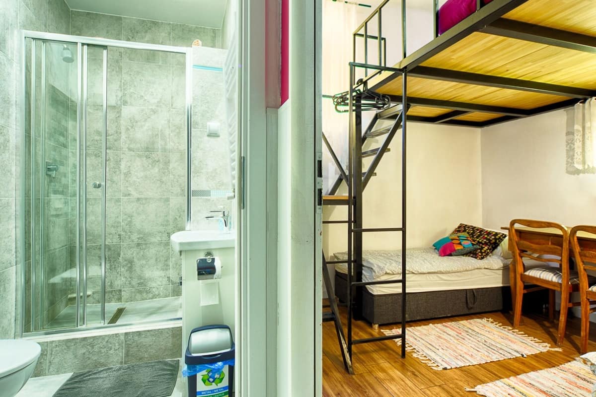 Une petite chambre comprenant un lit superposé, une douche et un petit espace bureau.