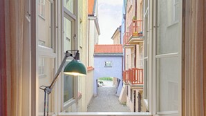 A narrow corridor with a wooden floor, a green desk lamp, and a view of a street with buildings and balconies.