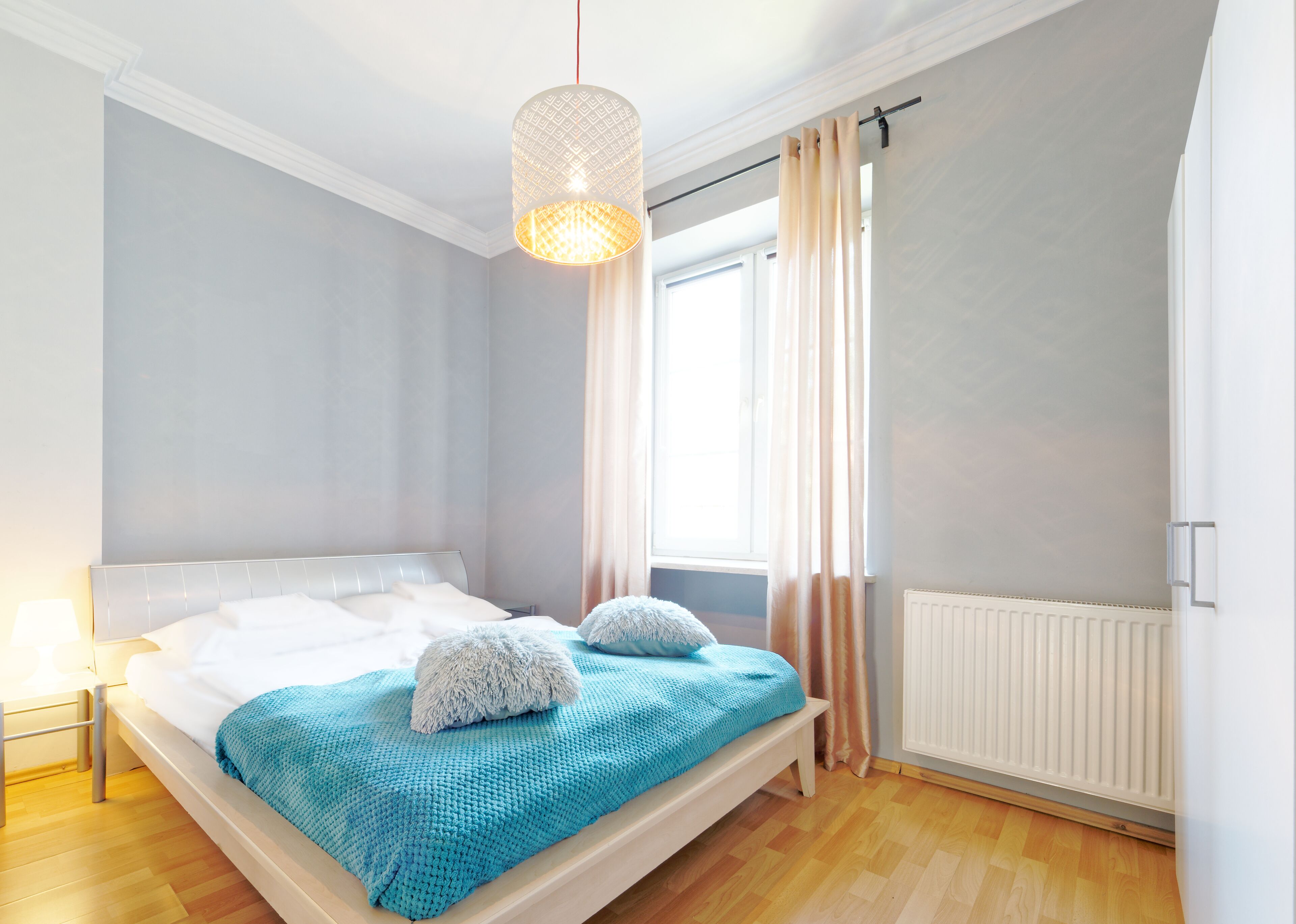 A bedroom with a bed, a hanging light fixture, a window with curtains, and a radiator.