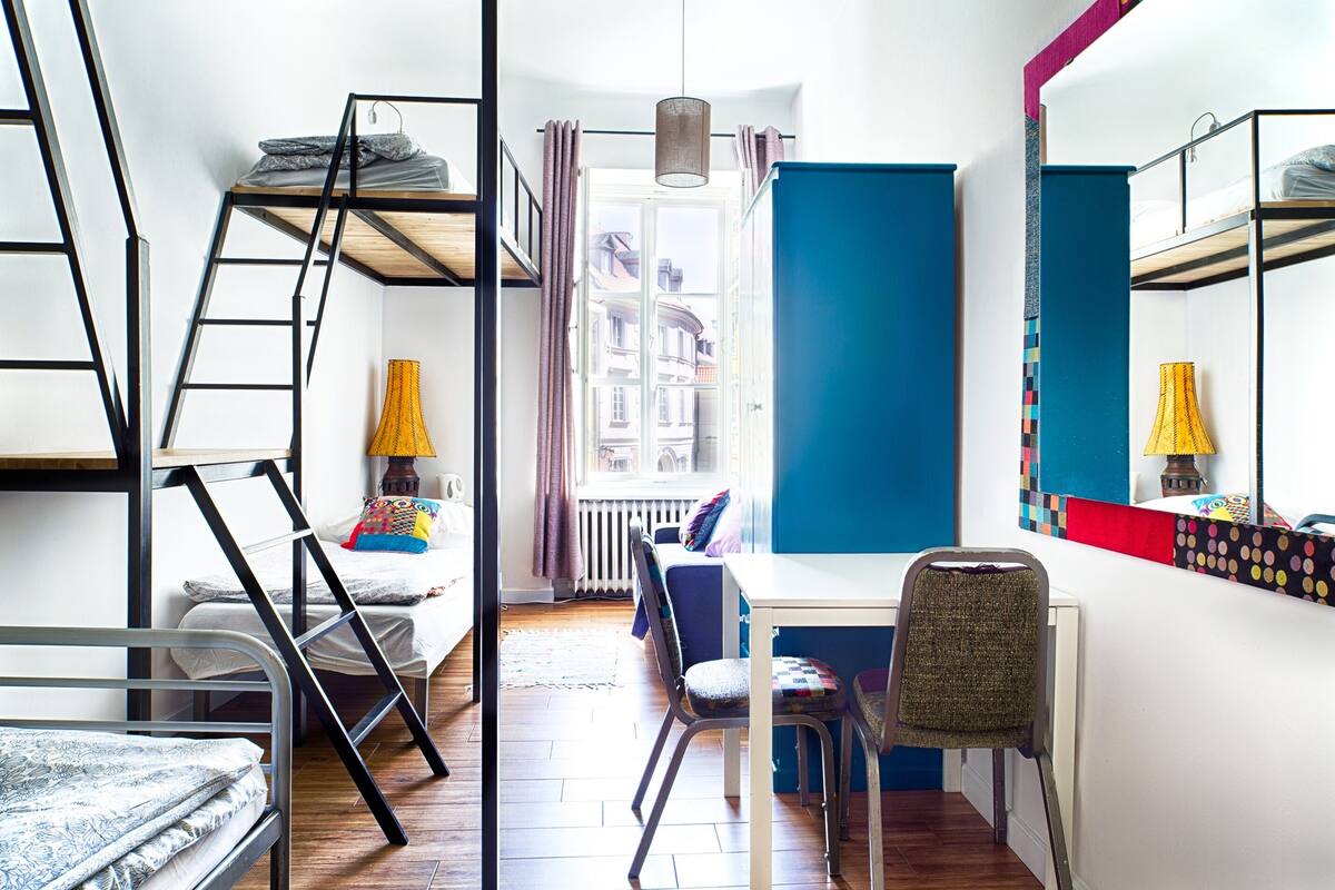 Une petite pièce avec des lits superposés, une petite table, une chaise et une fenêtre avec des rideaux.