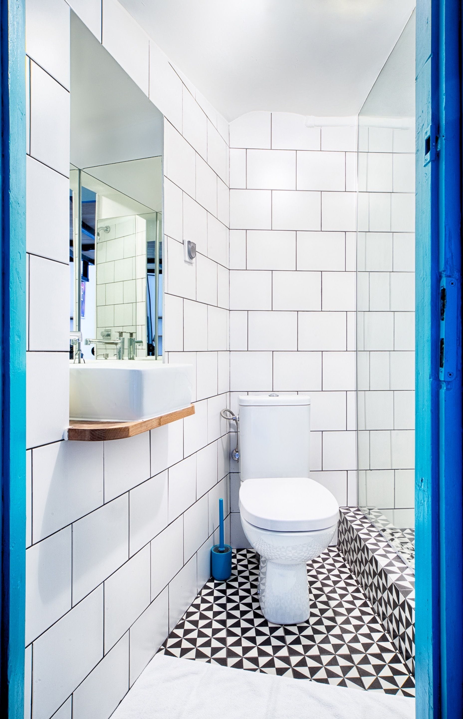 A bathroom with white tiles, a white toilet, a sink with a mirror, and a blue door.