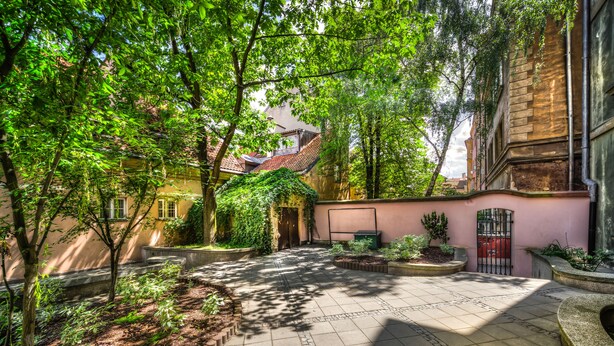 A courtyard with a tiled floor, surrounded by trees and plants, and buildings with a traditional architectural style.