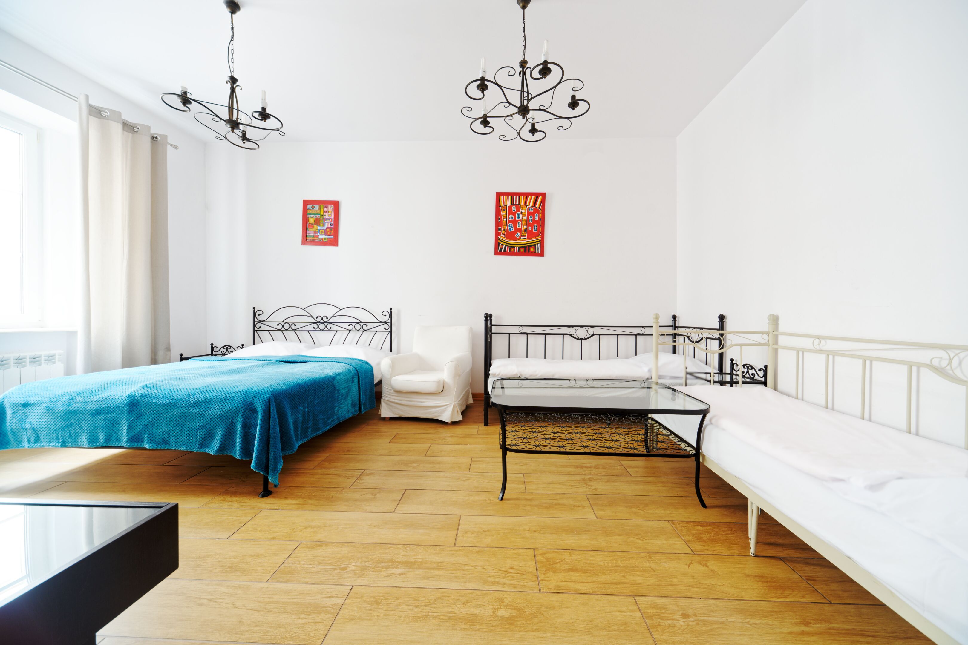A room with two beds, a chair, a table, and two chandeliers.