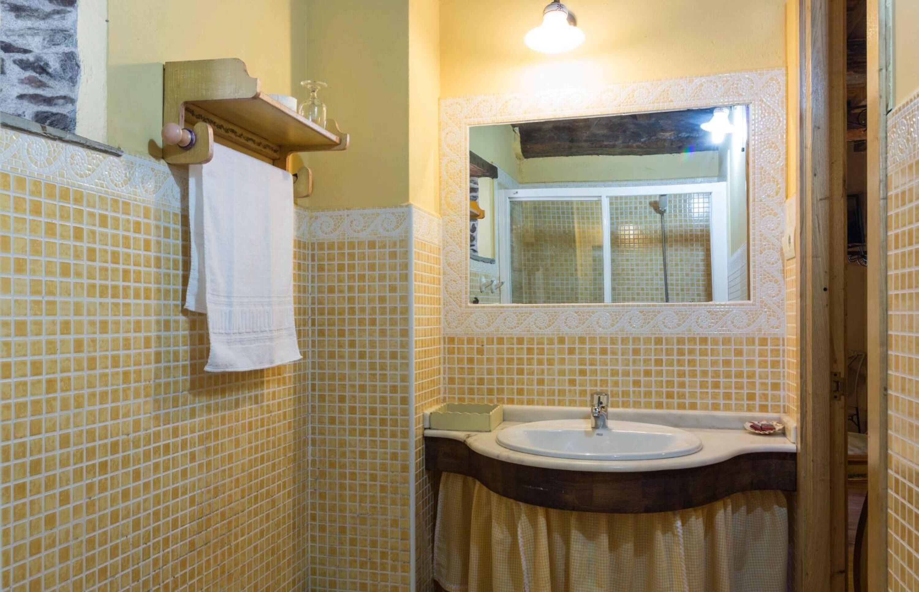 Un baño con paredes de azulejos amarillos, un mueble de tocador de madera, un lavabo y un espejo.