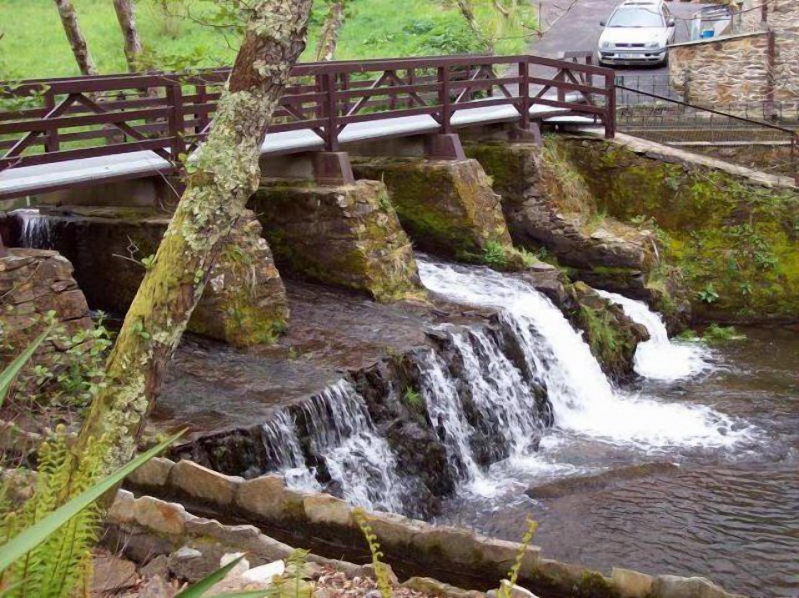 A waterfall with a wooden bridge and a stone wall.