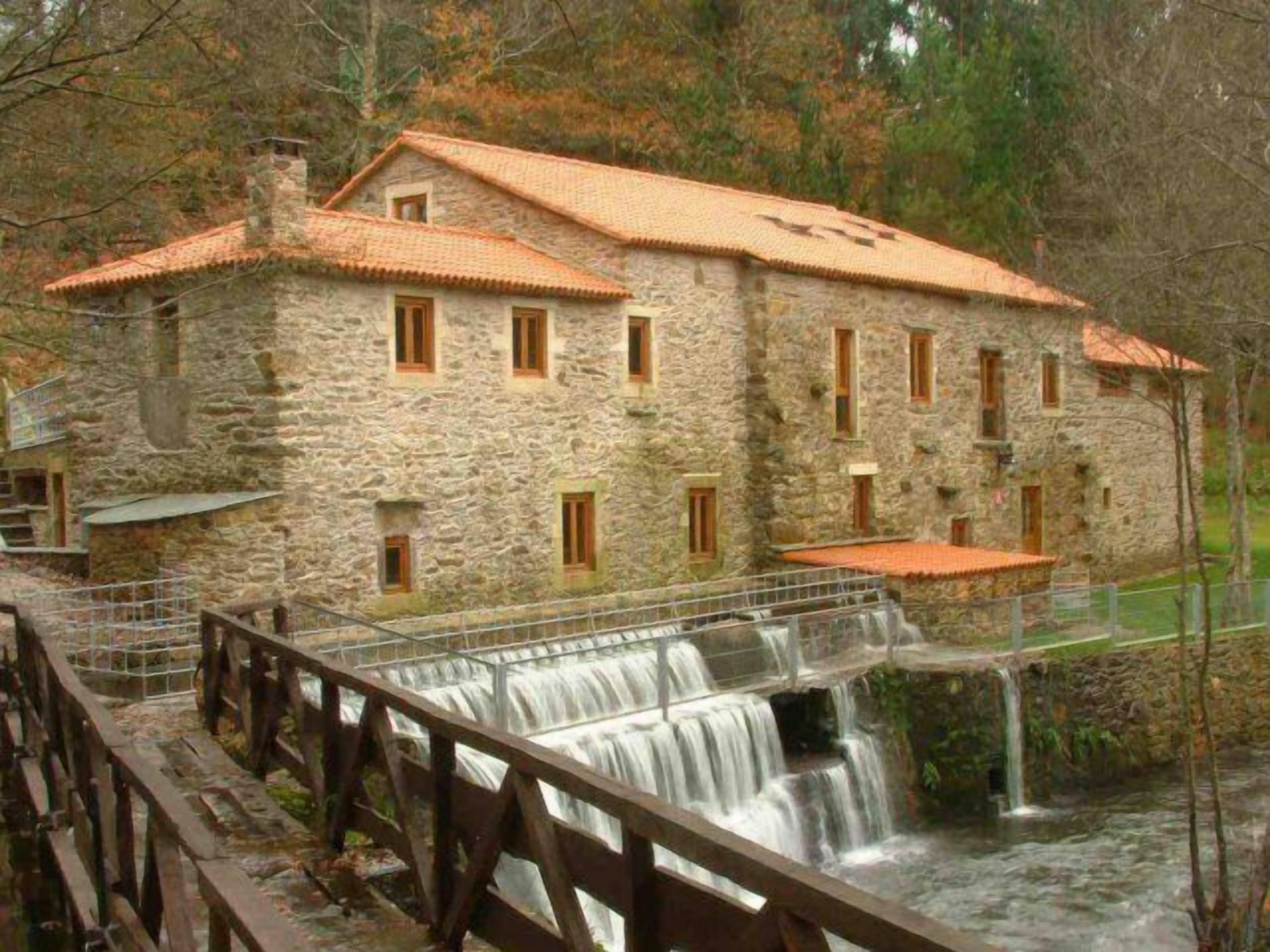 Un edificio de piedra con techo de tejas, una terraza de madera y una cascada.