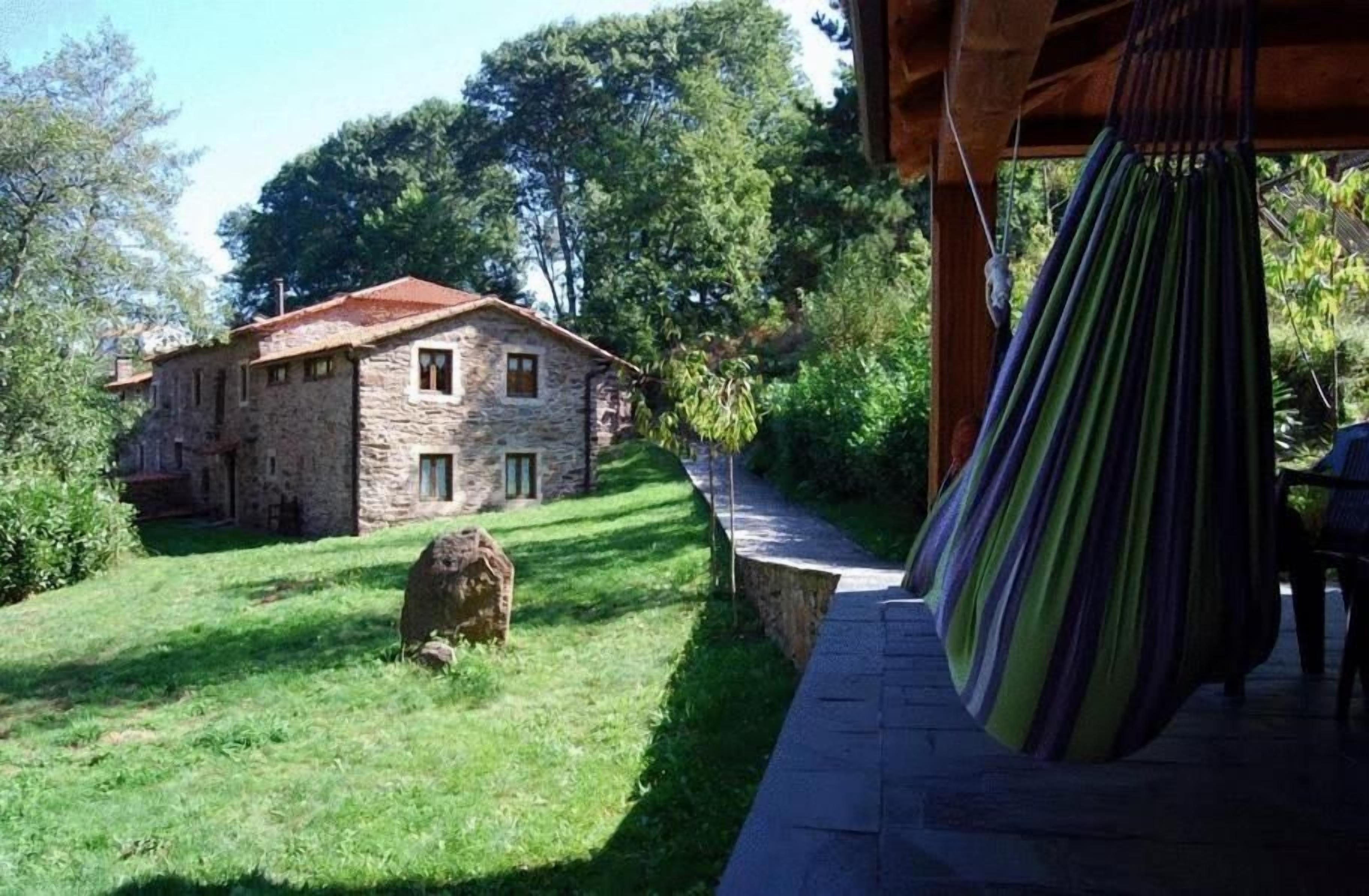 Un edificio de piedra con techo rojo, un patio cubierto de césped y una hamaca colgada de una estructura de madera.