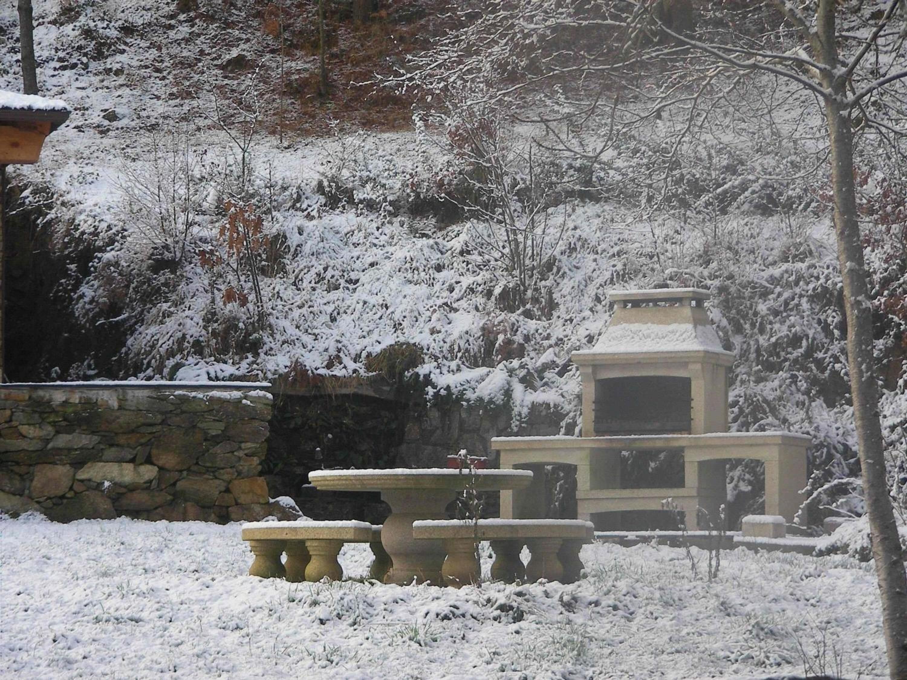 Un espacio al aire libre cubierto de nieve, con un muro de piedra, un banco de piedra y una pequeña construcción de piedra.