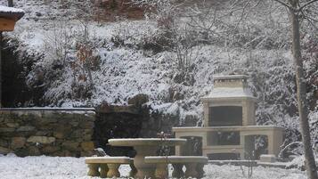 Un espacio al aire libre cubierto de nieve, con un muro de piedra, un banco de piedra y una pequeña construcción de piedra.