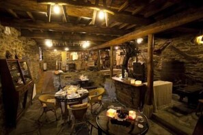 A rustic stone interior with a wooden ceiling, a round table with candles, and a stone fireplace. - O Muíño de Pena Casa Rural (O Pino)