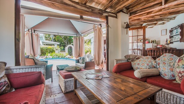 A cozy outdoor seating area with wicker furniture, a wooden table, and a view of a swimming pool. - HoneyPot Guesthouse (Umhlanga)