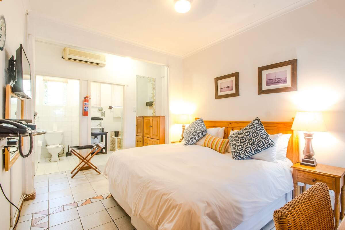 A hotel room with a large bed, two bedside lamps, a wooden headboard, and a wicker chair.