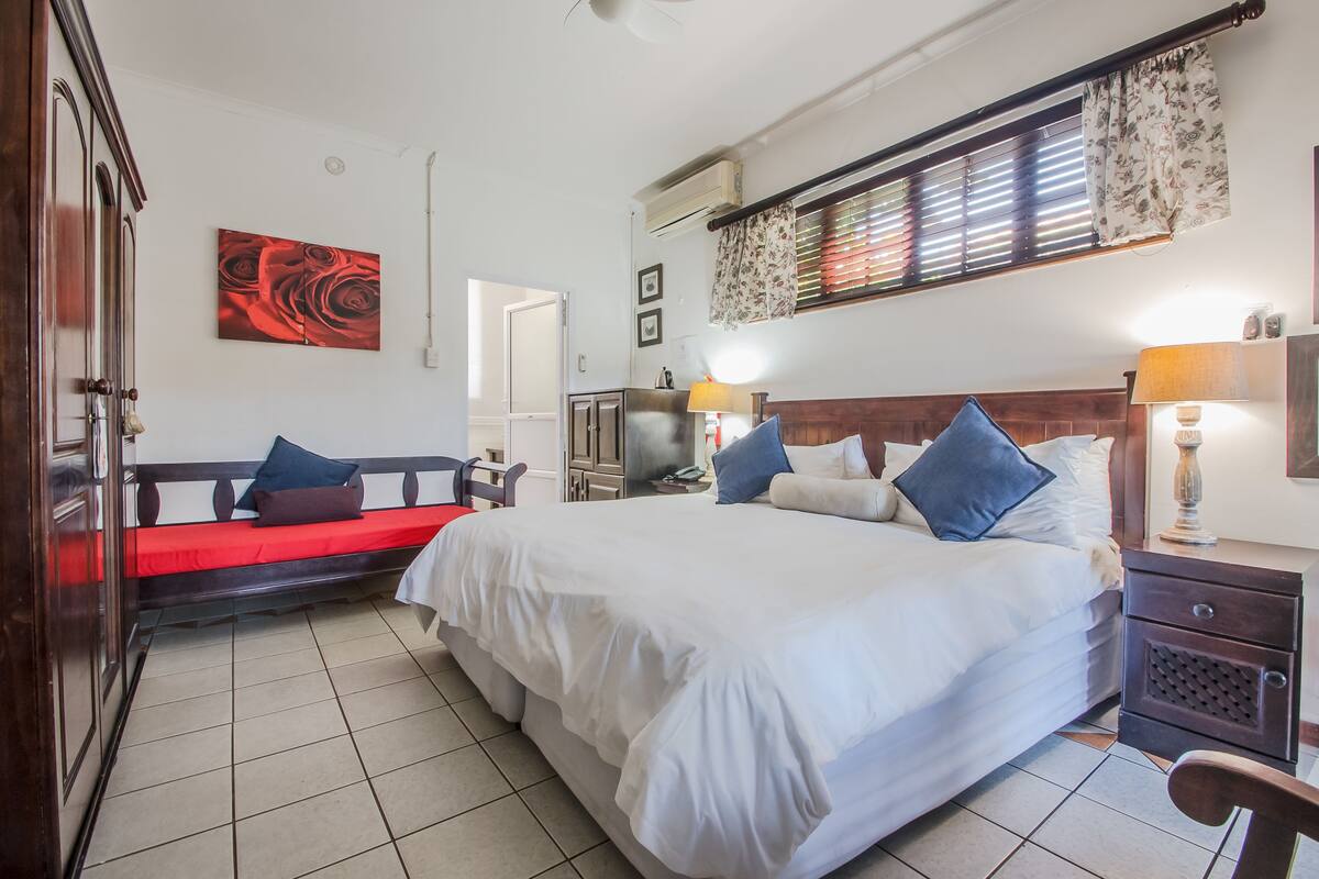 A bedroom with a large bed, a bench with cushions, a wardrobe, and a television.