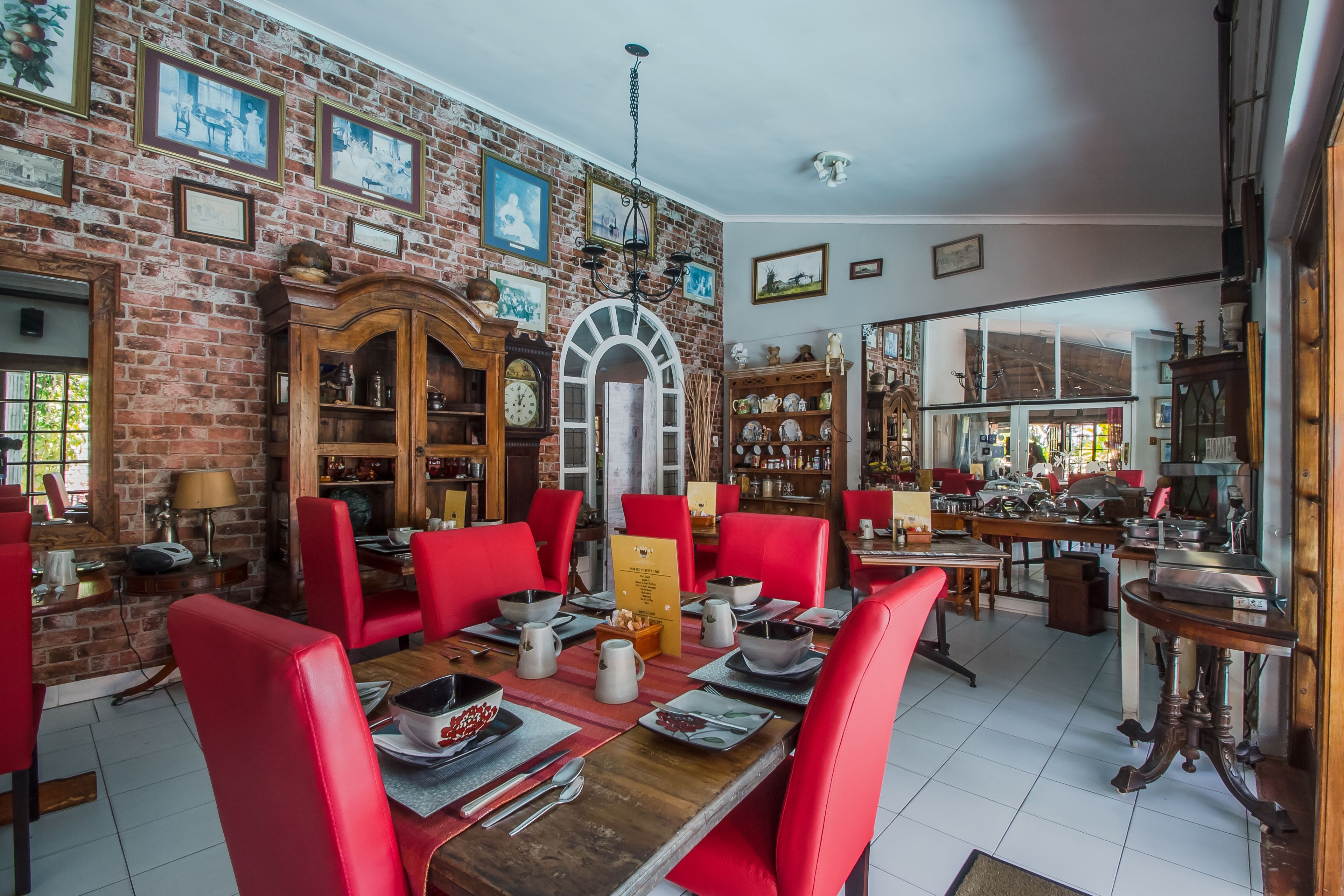 A dining area with red chairs, a wooden table, and a brick wall with framed pictures.