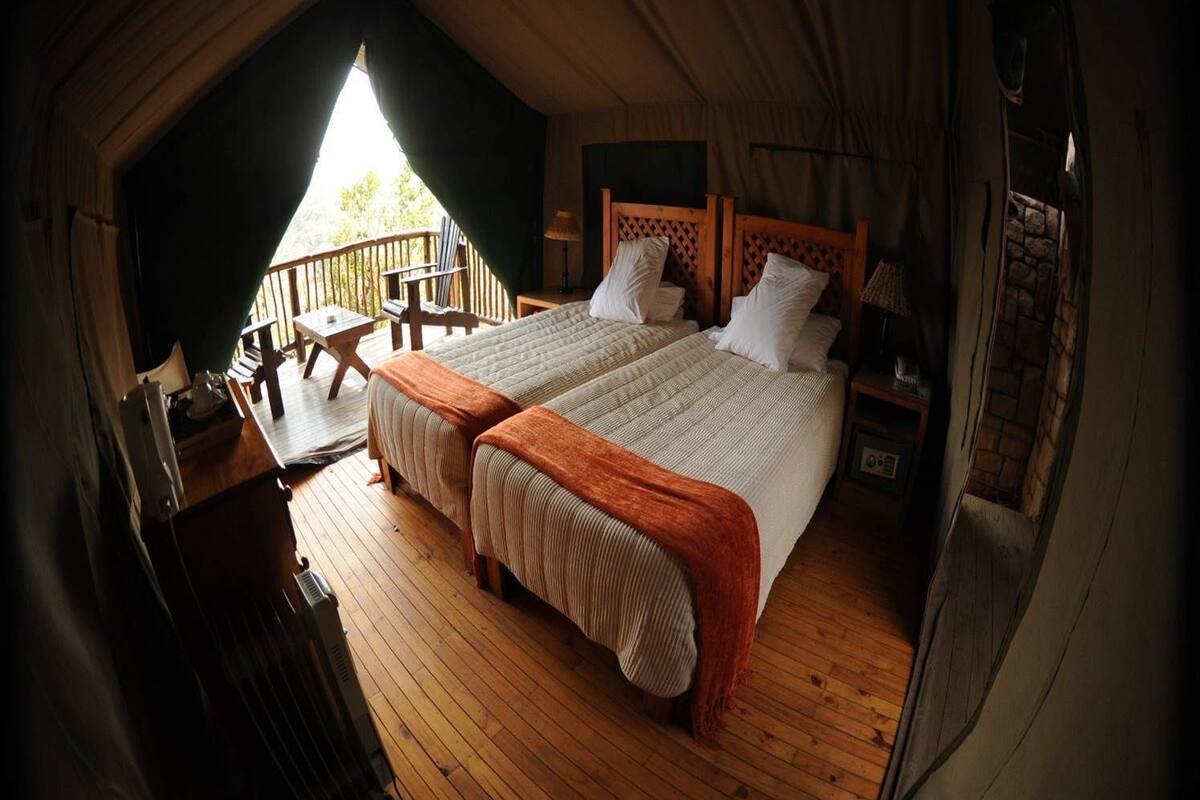 A cozy, well-lit tent-style room with two beds, a wooden deck, and a small table with chairs.