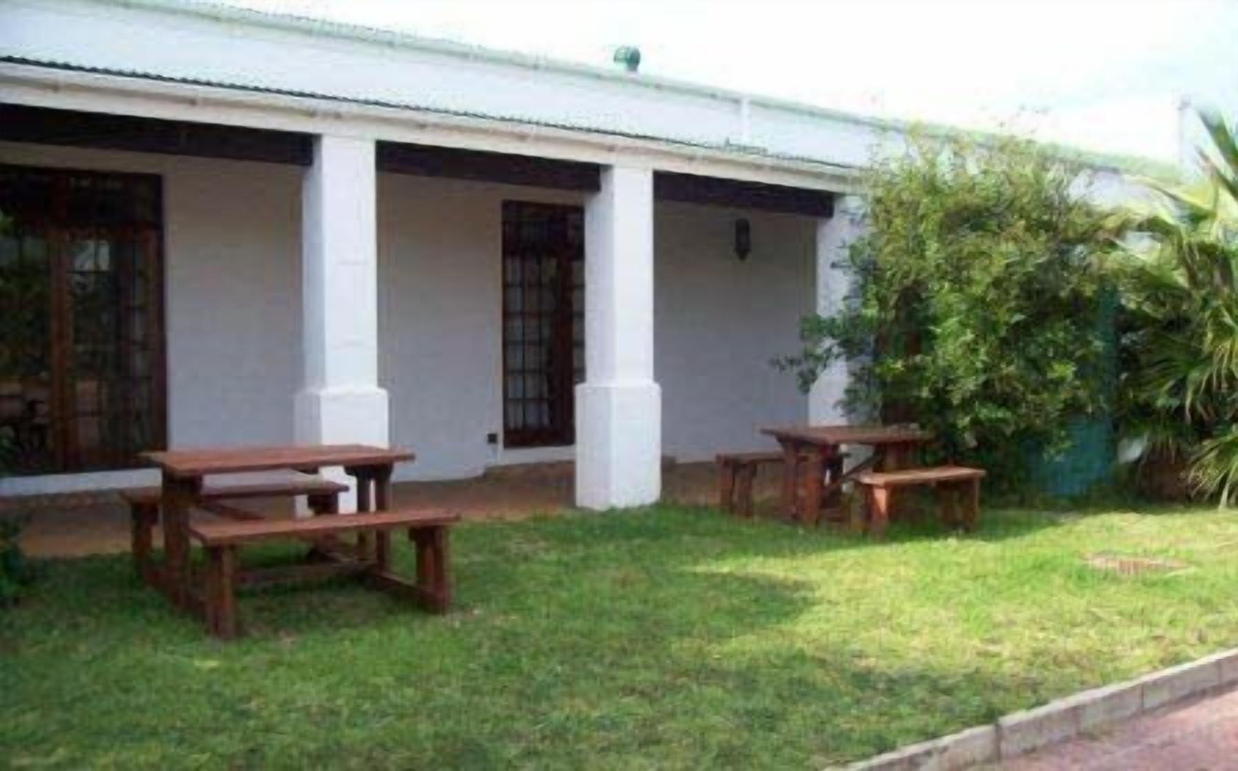 Un edificio con fachada blanca, columnas de madera y un porche cubierto con mesas de picnic.