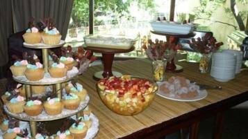 Una mesa de buffet con diversos alimentos, incluyendo cupcakes, un bol de fruta y un pastel.