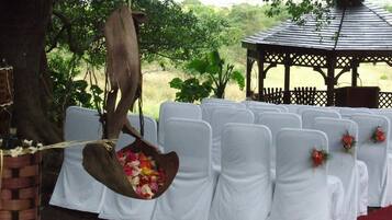 A gazebo with a wooden roof and lattice design, surrounded by white chairs with white tablecloths and floral centerpieces.