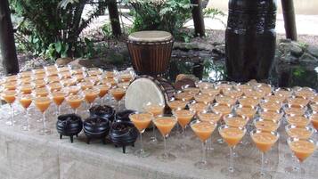 Une table dressée avec diverses boissons et de petits bols, entourée de plantes tropicales et d’une grande structure en pierre.