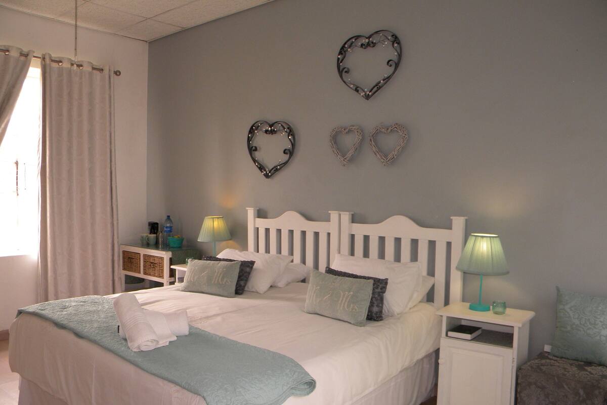 A neatly made bed with a white headboard, two bedside tables with lamps, and decorative heart-shaped wall art.