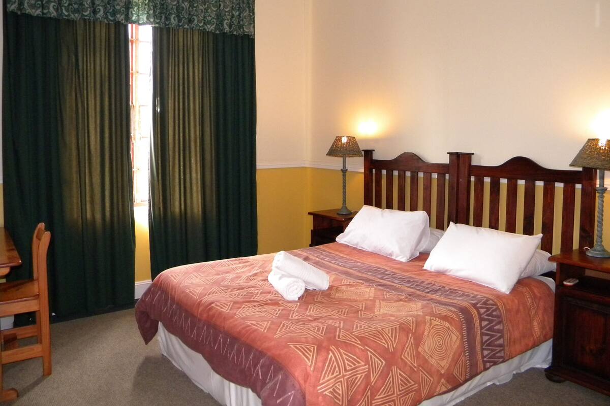 A neatly made bed with a patterned bedspread, two bedside lamps, and a wooden headboard.